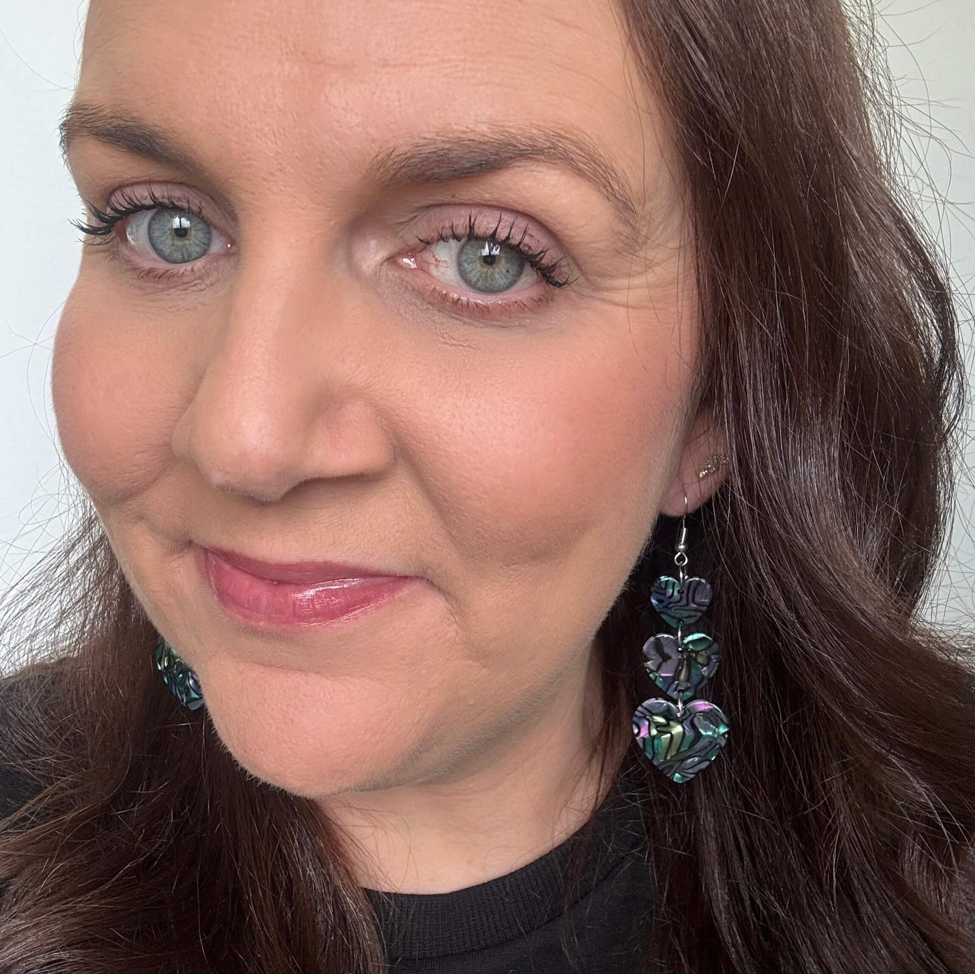 Close-up of a woman wearing opal earrings with a neutral background