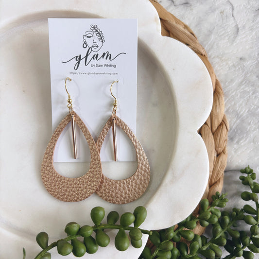 rose gold leather earrings on a white plate with a 'glam by Sam Whiting' card, surrounded by greenery.
