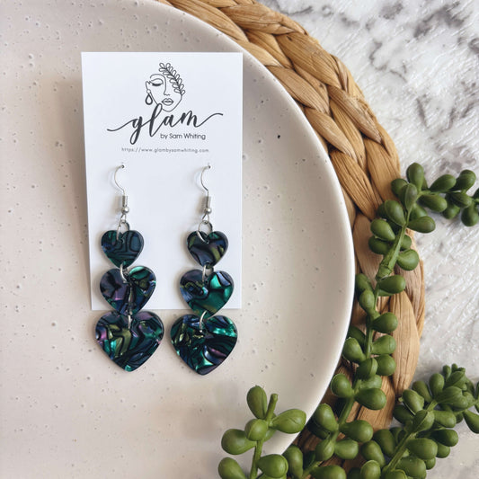Opal heart-shaped earrings on a Glam by Sam Whiting card with greenery around.
