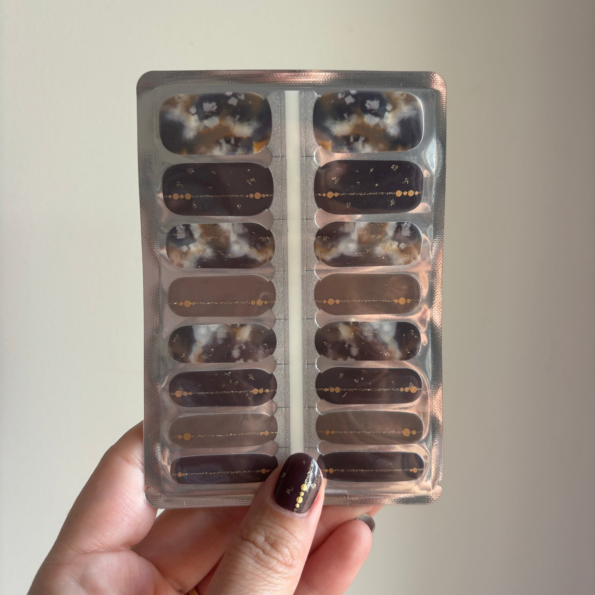 Hand holding a nail polish strip set with a marble pattern against a plain background
