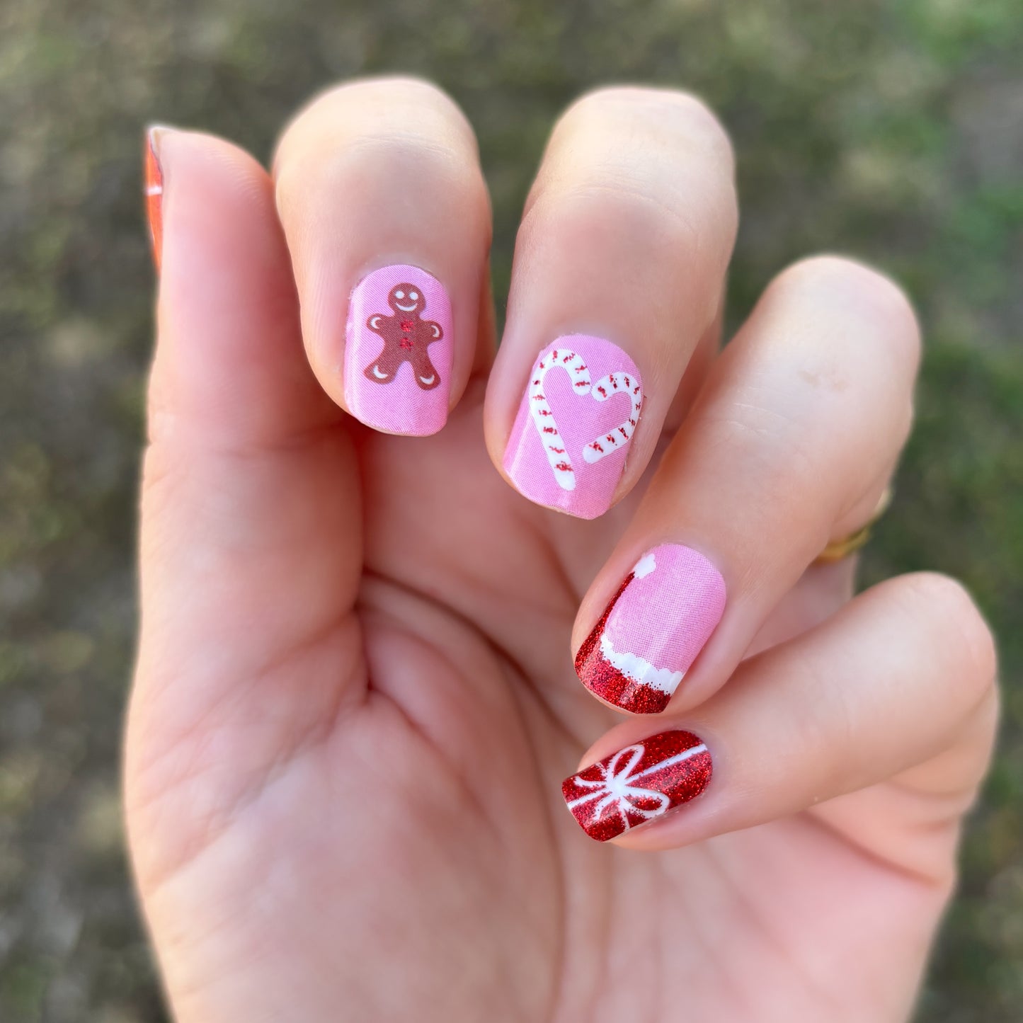 Hand with pink Christmas-themed nail art on a blurred natural background