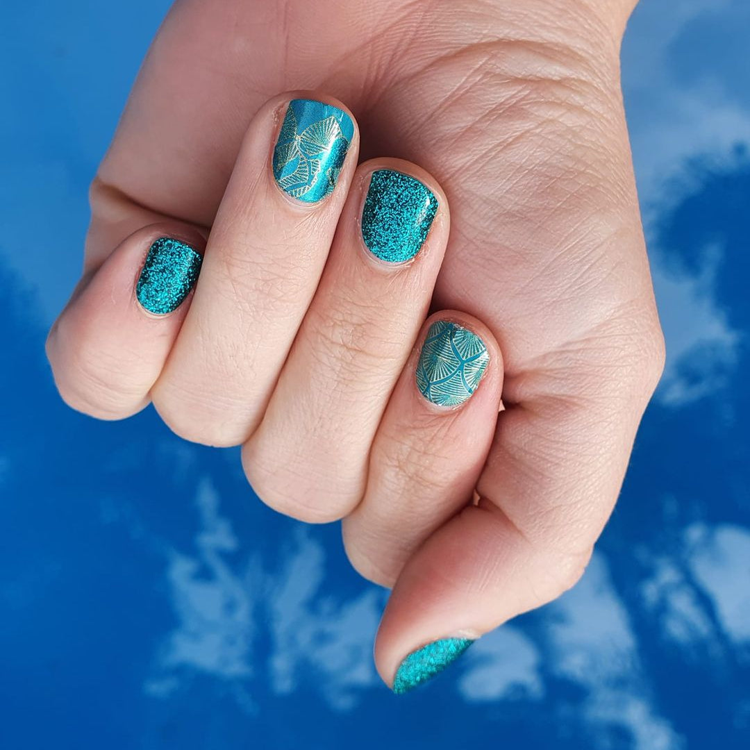 Hand with turquoise glittery nail polish against a blue water background