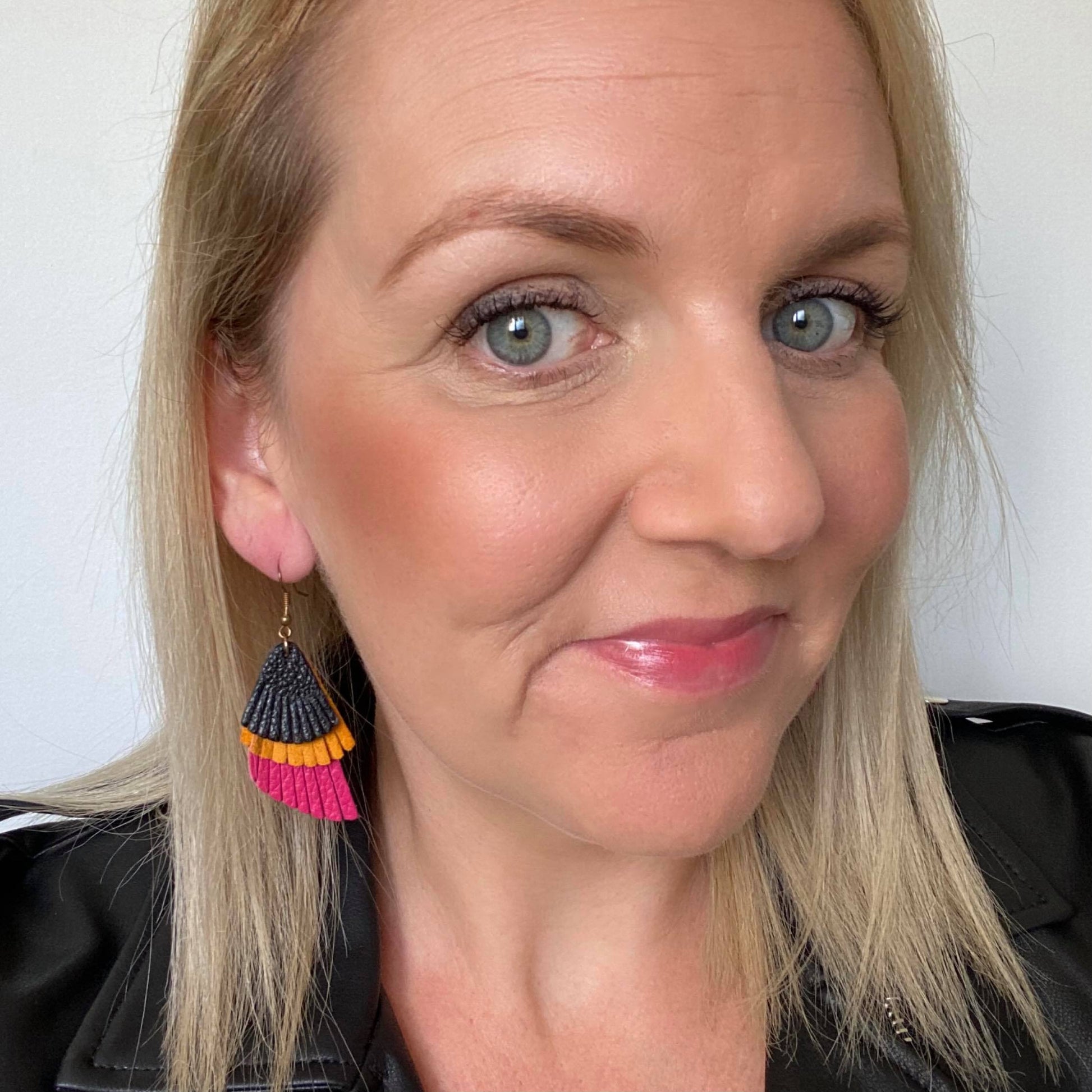 Selfie of colour blocked, triple layer feathered leather earrings featuring a gold coloured hook.