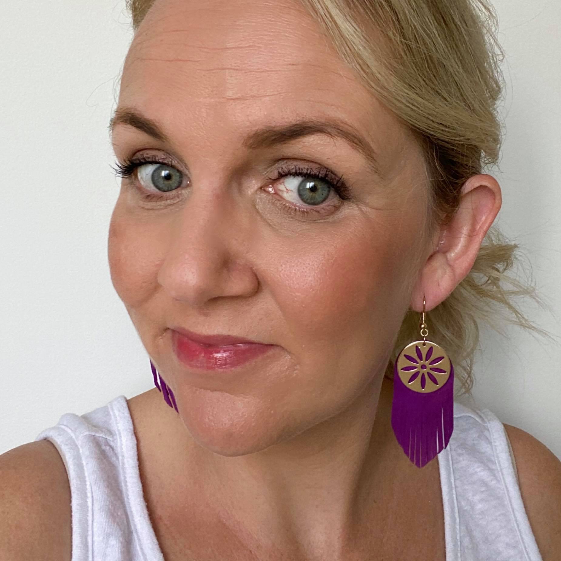 selfie of purple fringe leather earrings featuring a gold coloured embellishment and hook
