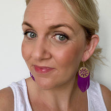 Load image into Gallery viewer, selfie of purple fringe leather earrings featuring a gold coloured embellishment and hook
